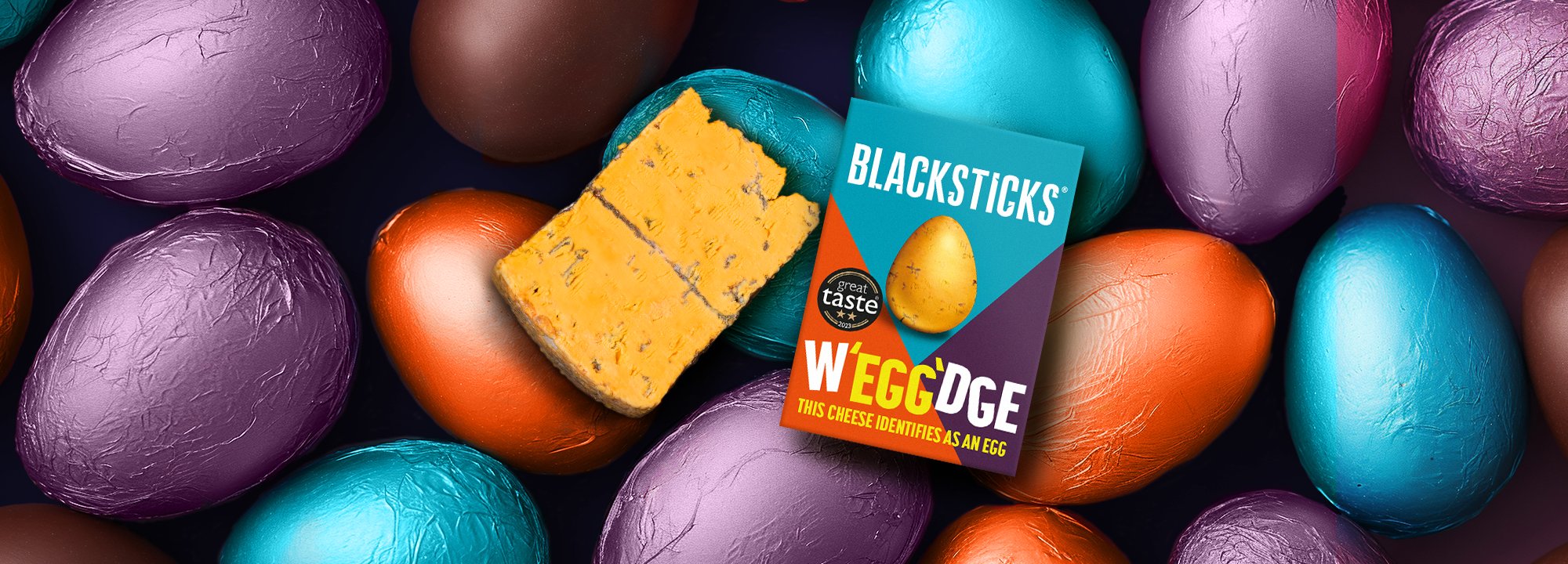 Easter eggs in background with a wedge of Blackstick blue cheese on top and W'egg'dge packaging.s 