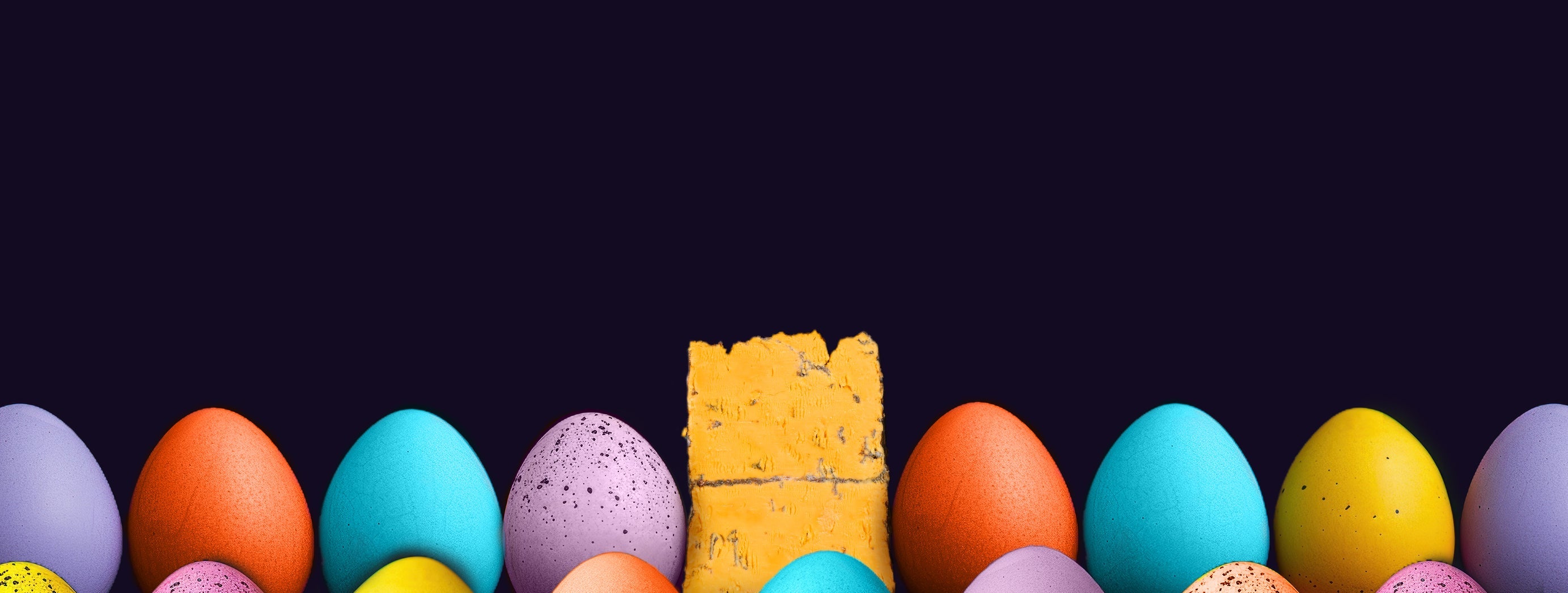 Easter eggs in background with a wedge of Blackstick blue cheese on top and W'egg'dge packaging.s 