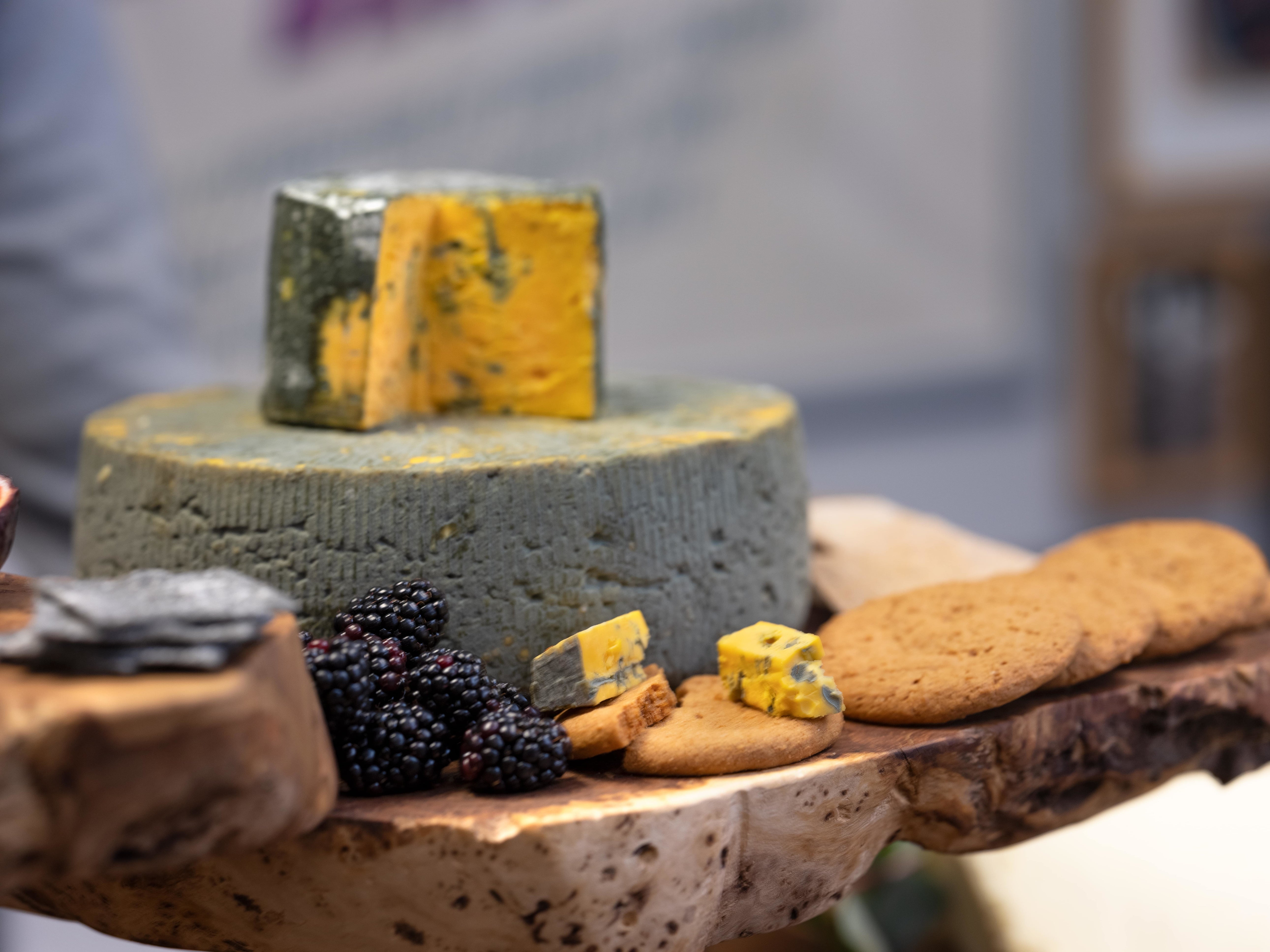 Celebration cheese, a Blacksticks Blue cheese wheel on a wooden cheese board with fruit and crackers.