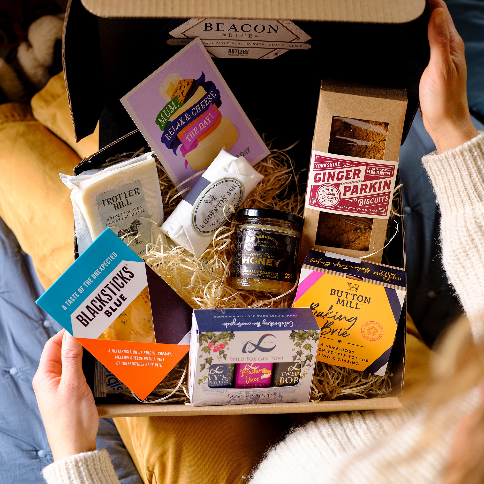 Mother's Day Cheese Hamper | Four cheese selection to make a cheeseboard, biscuits, honey and Wildfox Gin Trio being opened on someones lap.