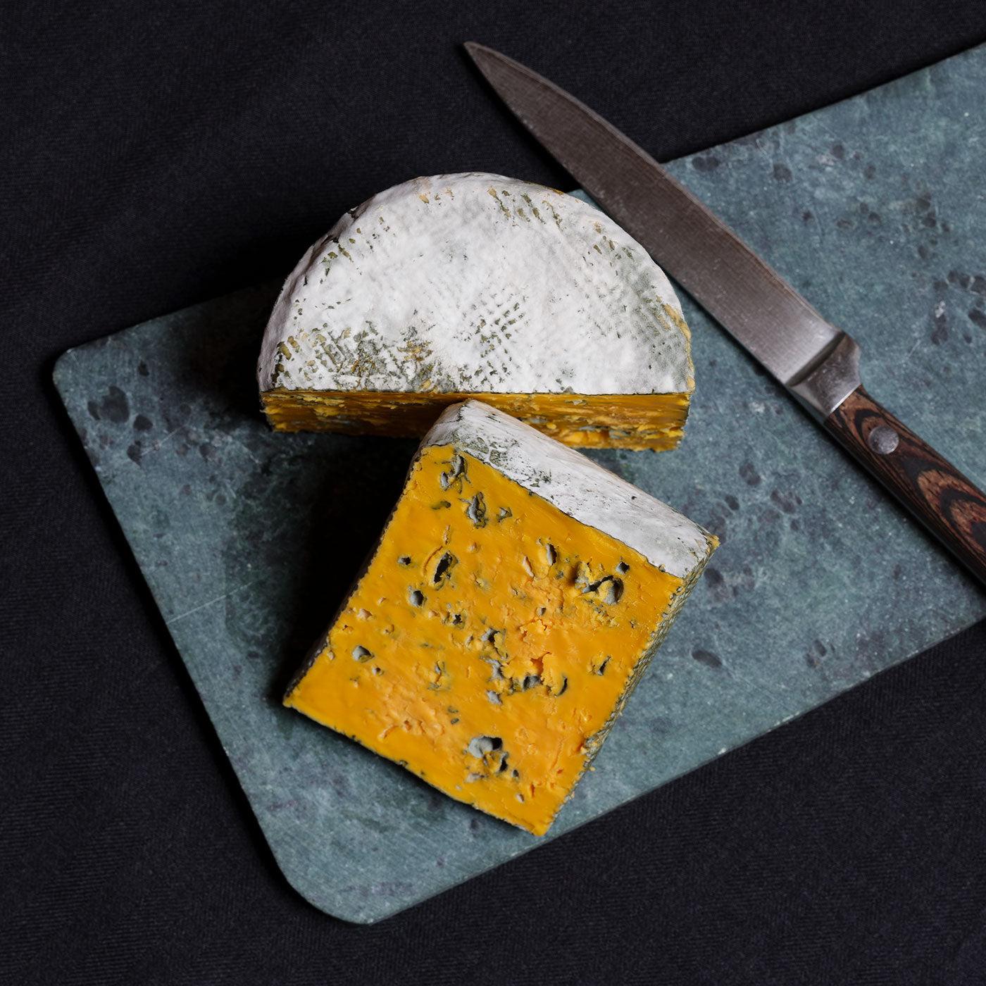 Whole Mini Baby Blacksticks Blue Cheese Truckle sliced up on a cheeseboard.