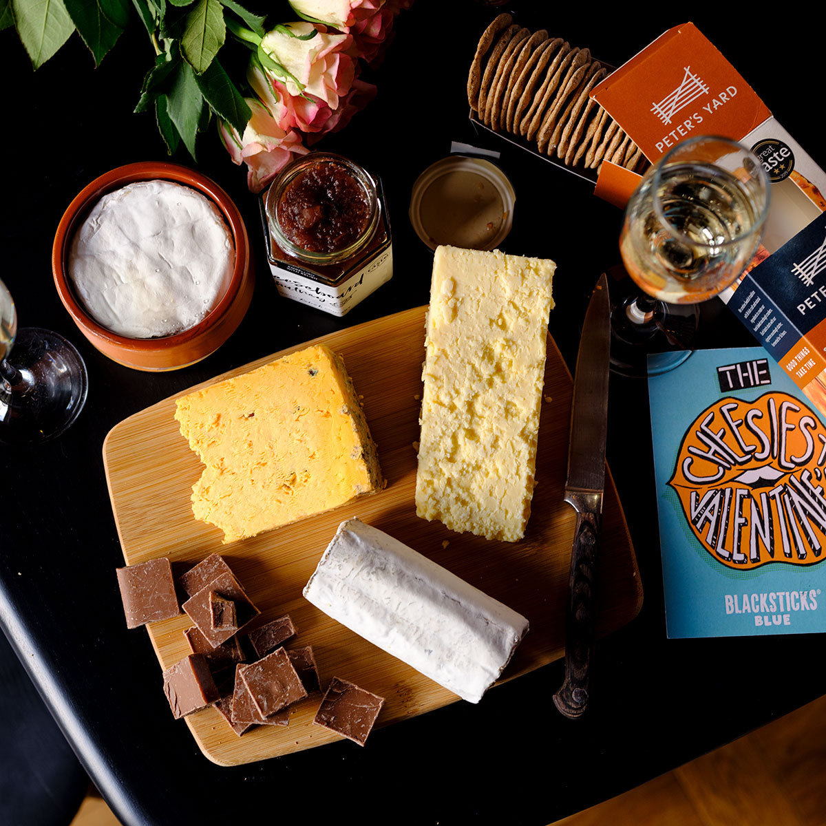 The Ultimate Valentine's Day Cheese Hamper | Overhead shot of three cheeses on a cheeseboard with chutney, crackers, Valentines card, baking brie and champagne.