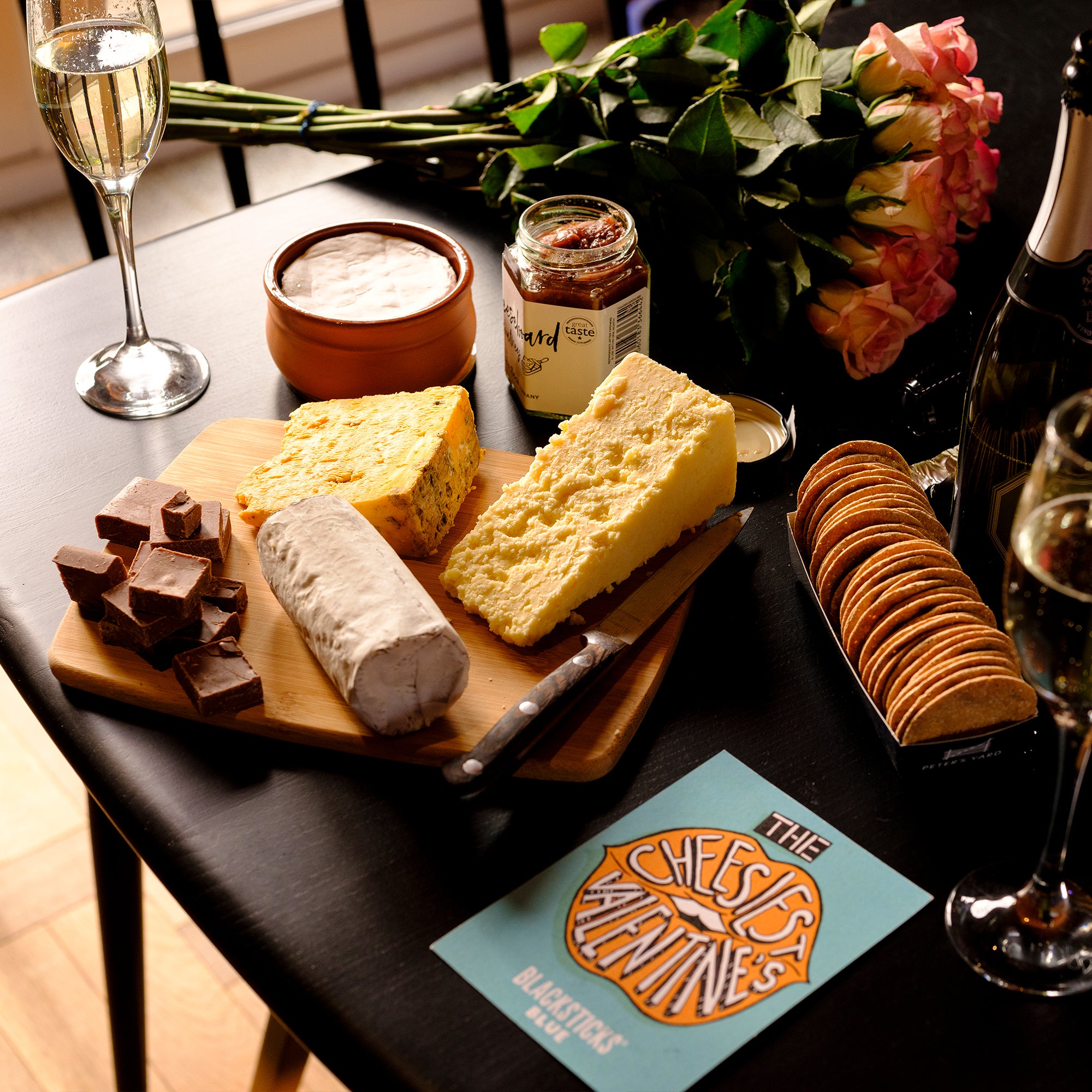Serving suggestion for our Ultimate Valentine's Day Cheese Hamper on a cheeseboard with flowers and champagne | Cheese Gifts