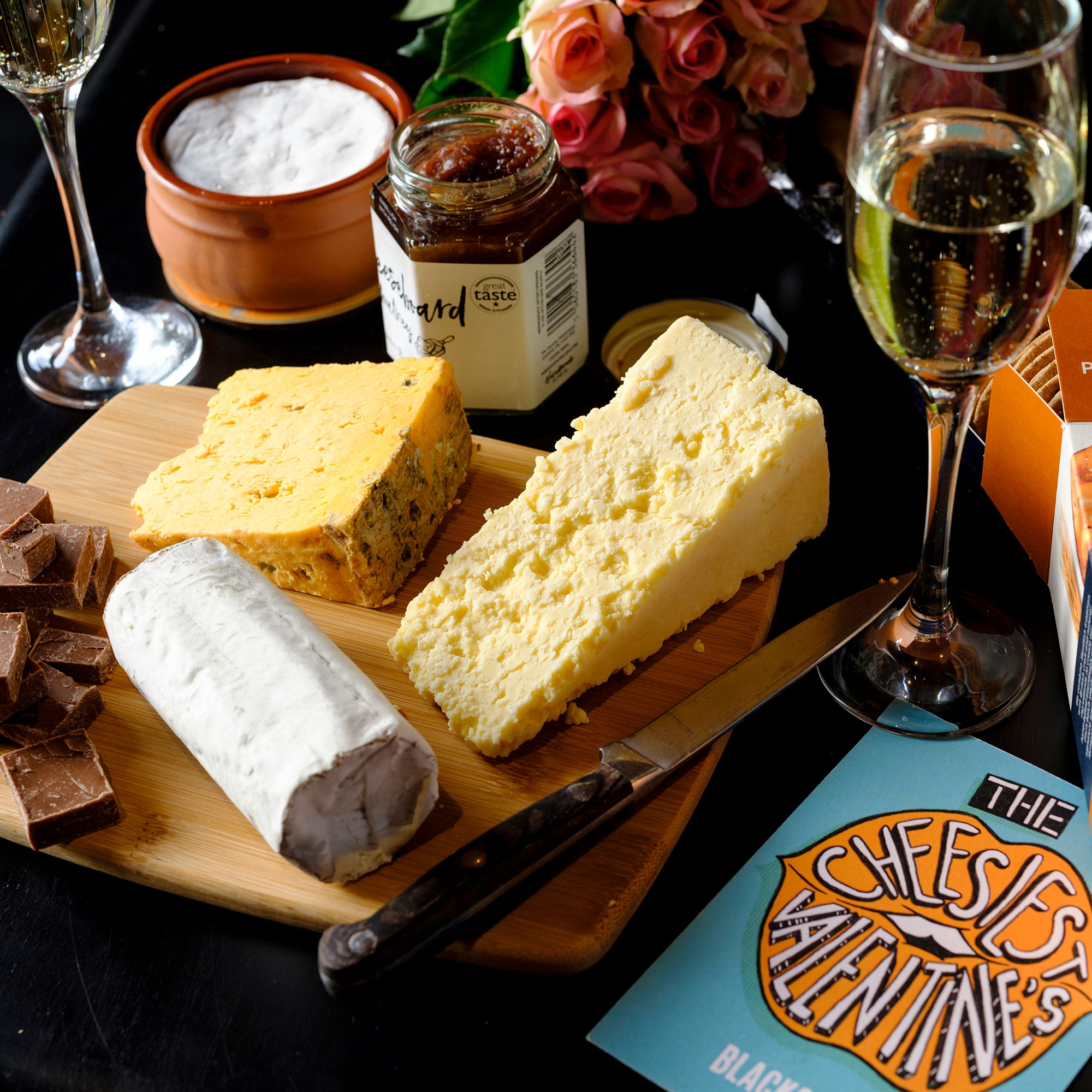 The contains of our Ultimate Valentine's Day Cheese Hamper, with three cheeses on a cheeseboard with chutney, crackers, Valentines card, baking brie and champagne.